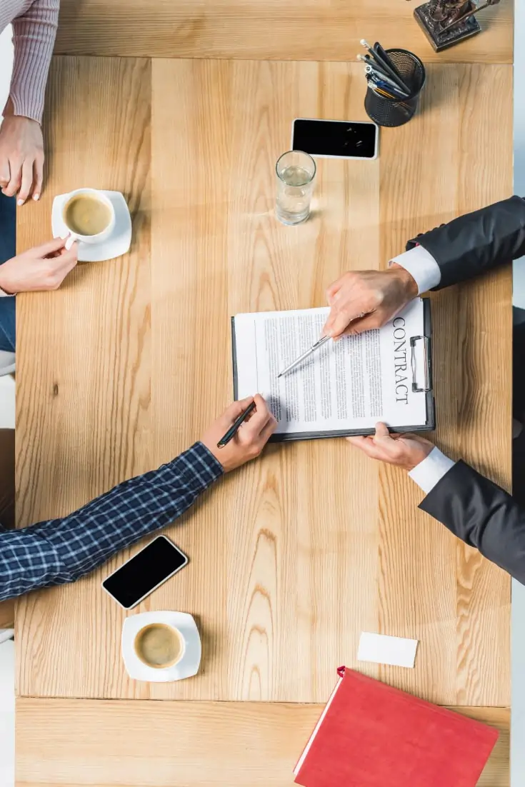 Legal Dalal – Businessmen shaking hands to sell a company, with legal documents and laptop on desk during a company ownership transfer.